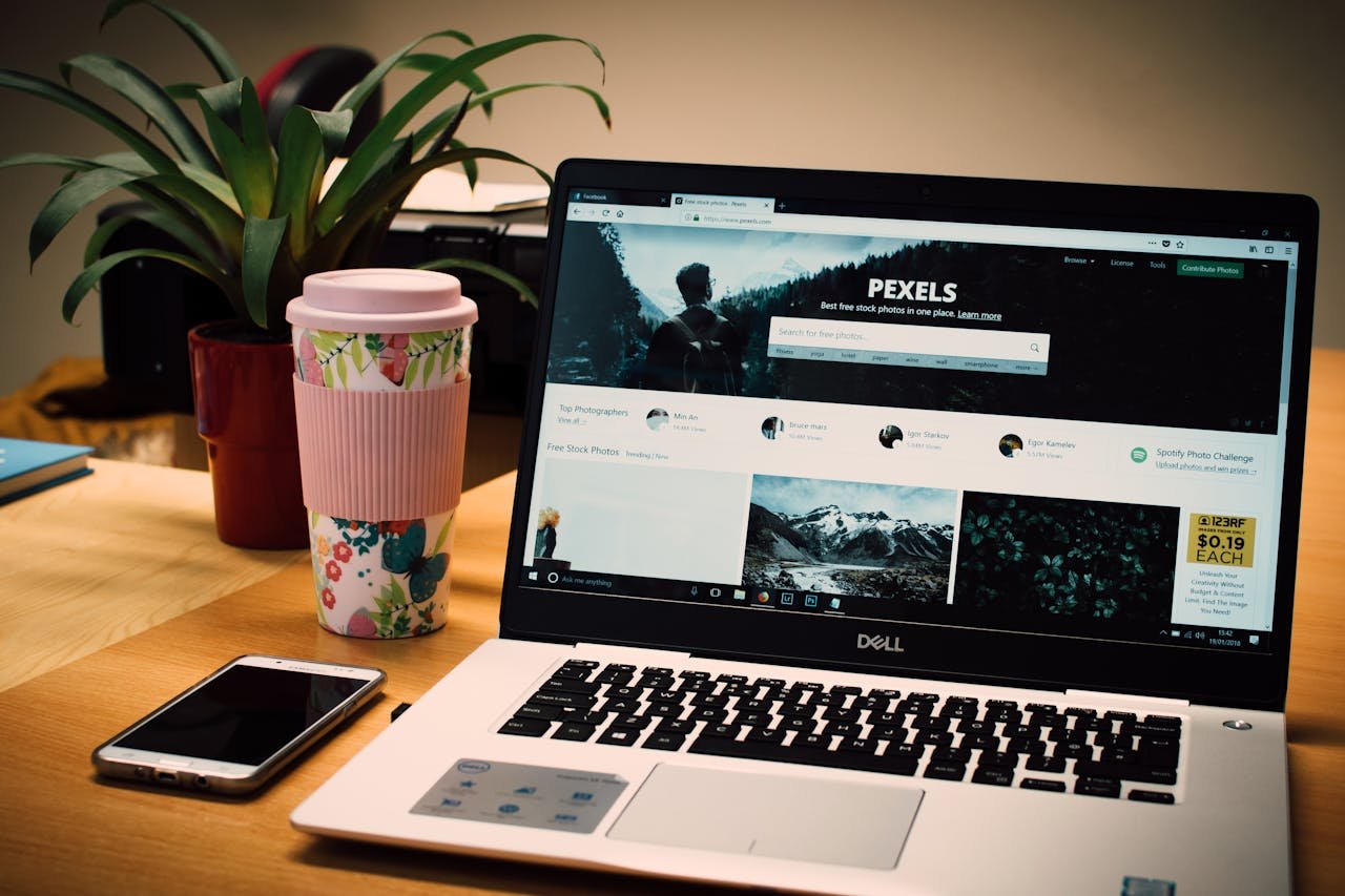 A tidy desk setting with a laptop showing a stock photo website and a smartphone.